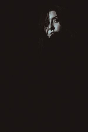 A dark artistic portrait with dramatic side lighting and shadows creating a moody atmospheric effect.