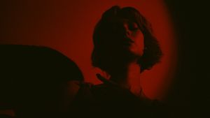 A dramatic silhouetted figure stands against a dark red background with atmospheric lighting effects.