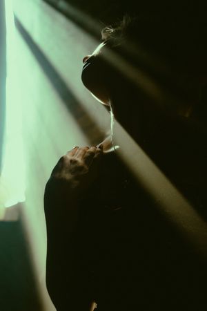 A silhouette in dramatic lighting creates a moody atmosphere with beams of light cutting through darkness.