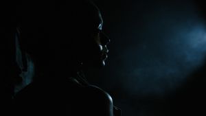 A dark silhouette of a person stands against a deep blue atmospheric background with dramatic lighting effects.