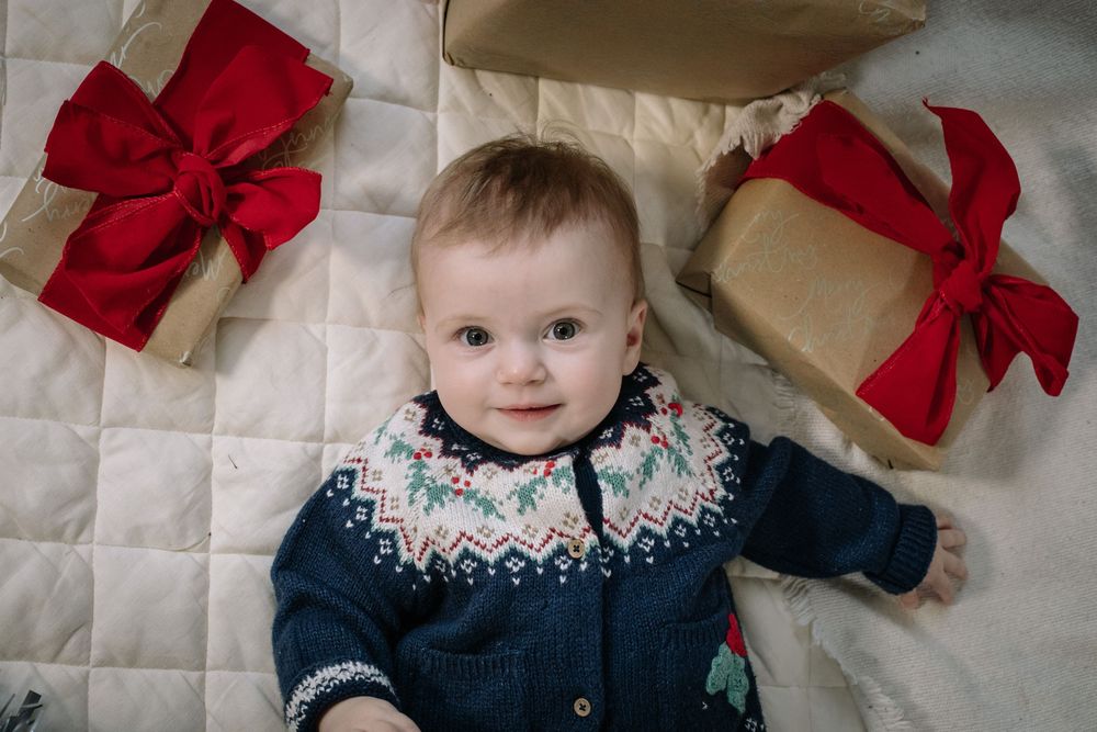 Holiday portrait with navy fair isle sweater lying on quilted surface next to wrapped presents with red bows.