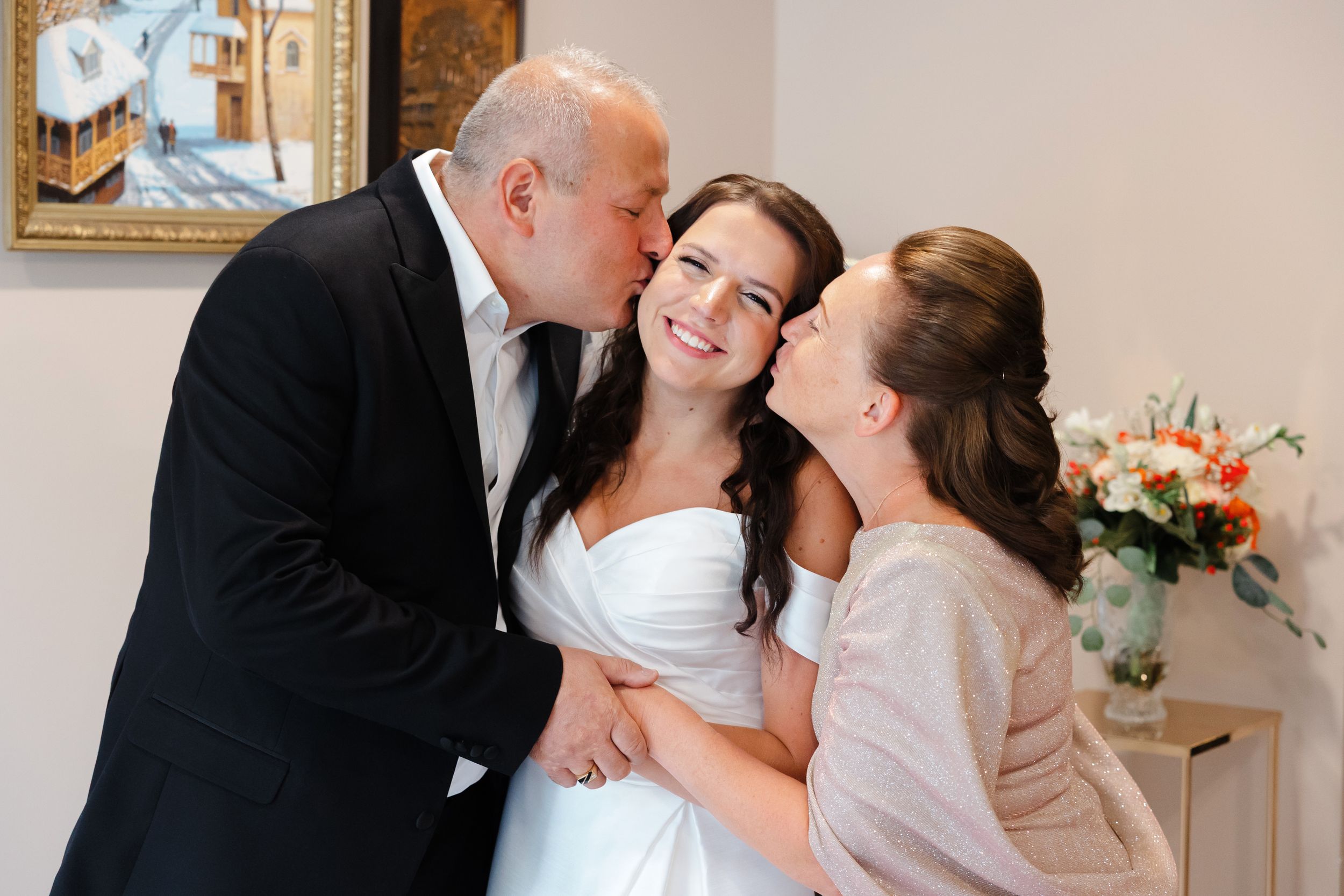 Bride's parents kissing her before leaving for wedding day.