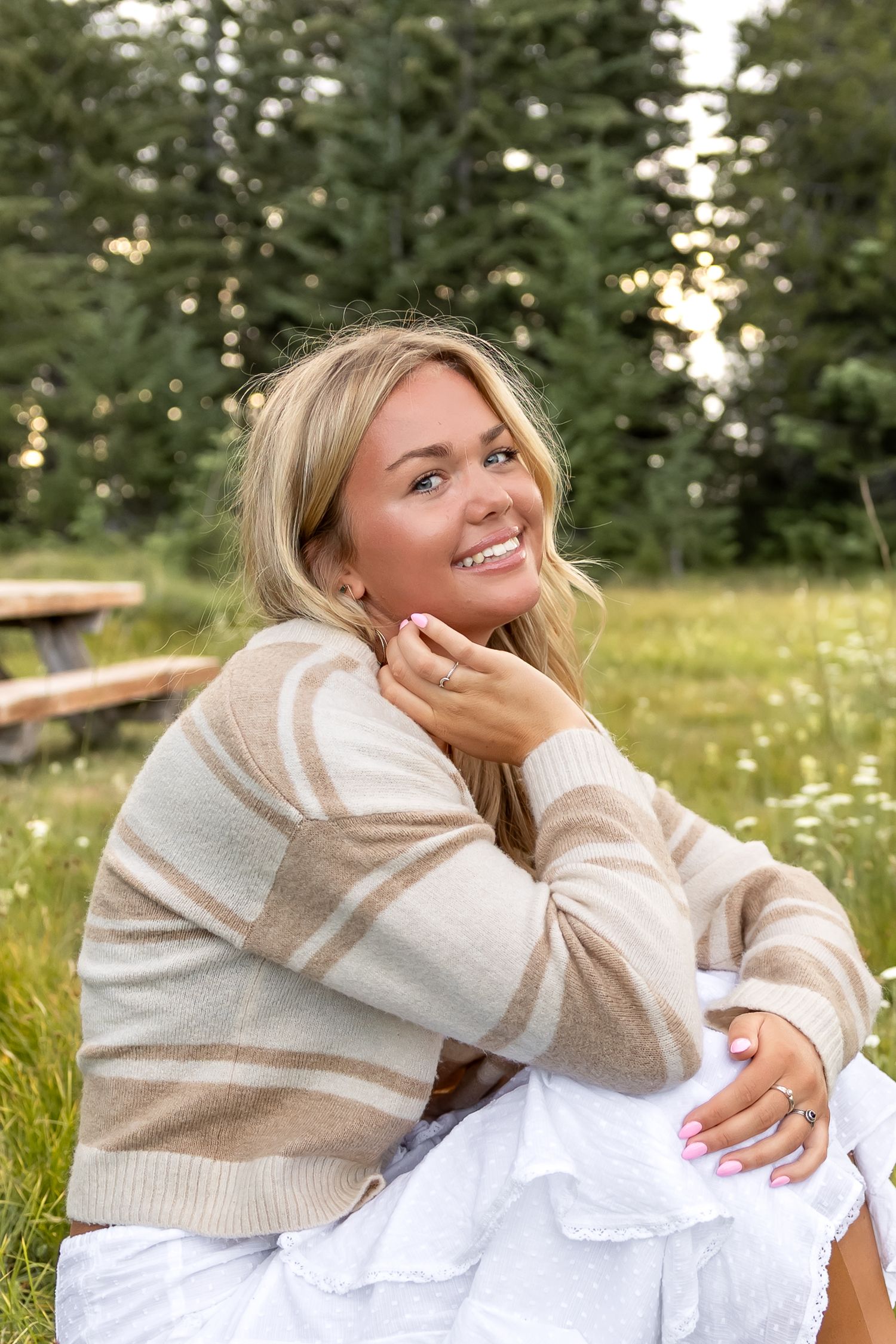A person in a beige sweater and white dress sits in a grassy field on a sunny summer day.