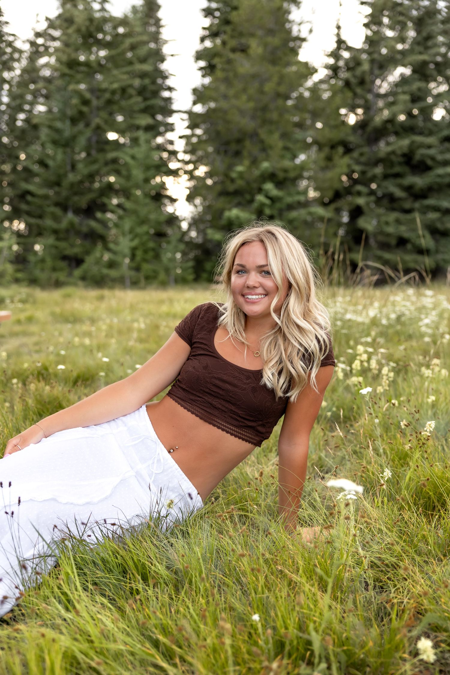 A summer photo shoot in a meadow with wildflowers and tall grass against a backdrop of evergreen trees.