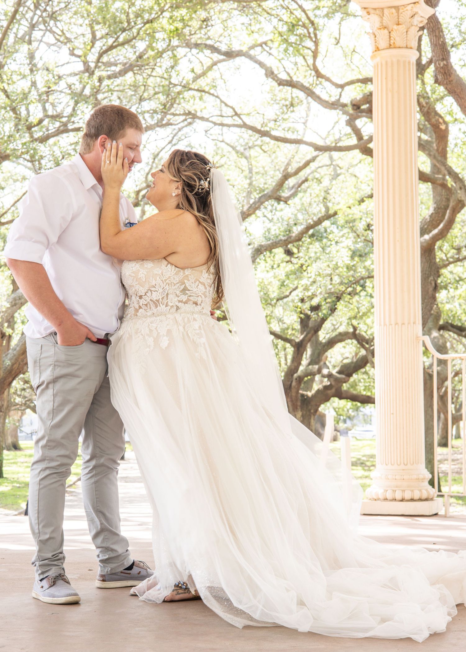 Romantic couple dancing together on an elegant columned porch with sunlit trees in the background.