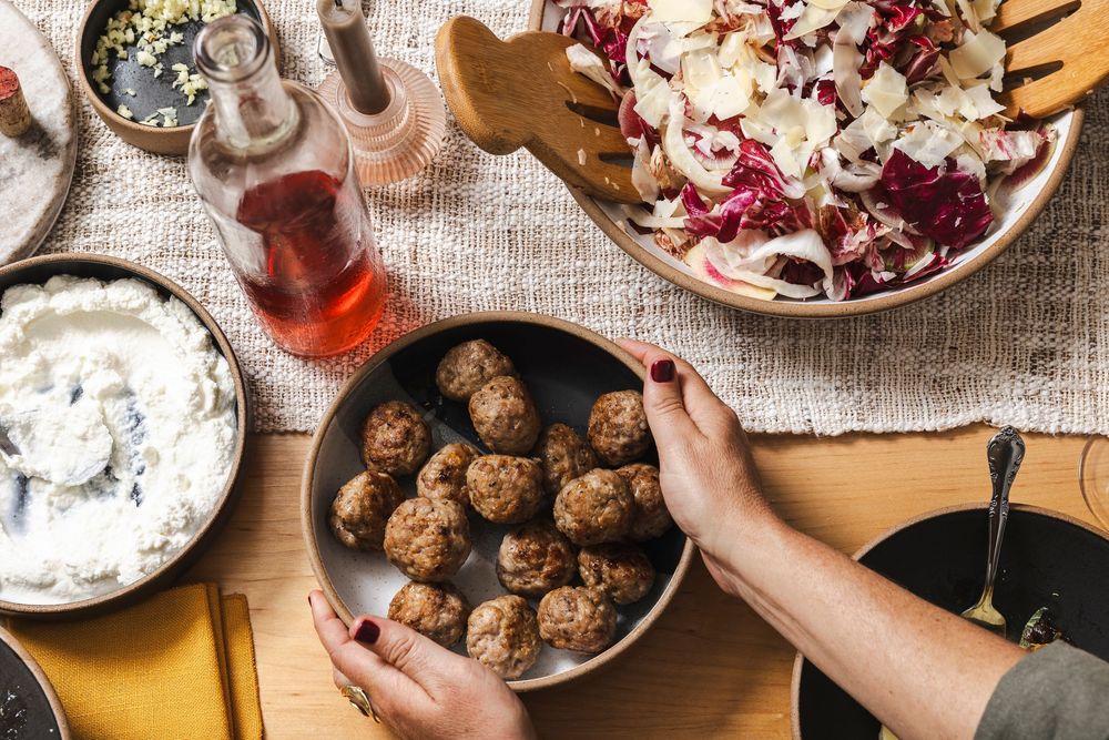 Overhead view of meatballs, salad, and dipping sauce being served on a rustic table setting with a glass of rose wine.