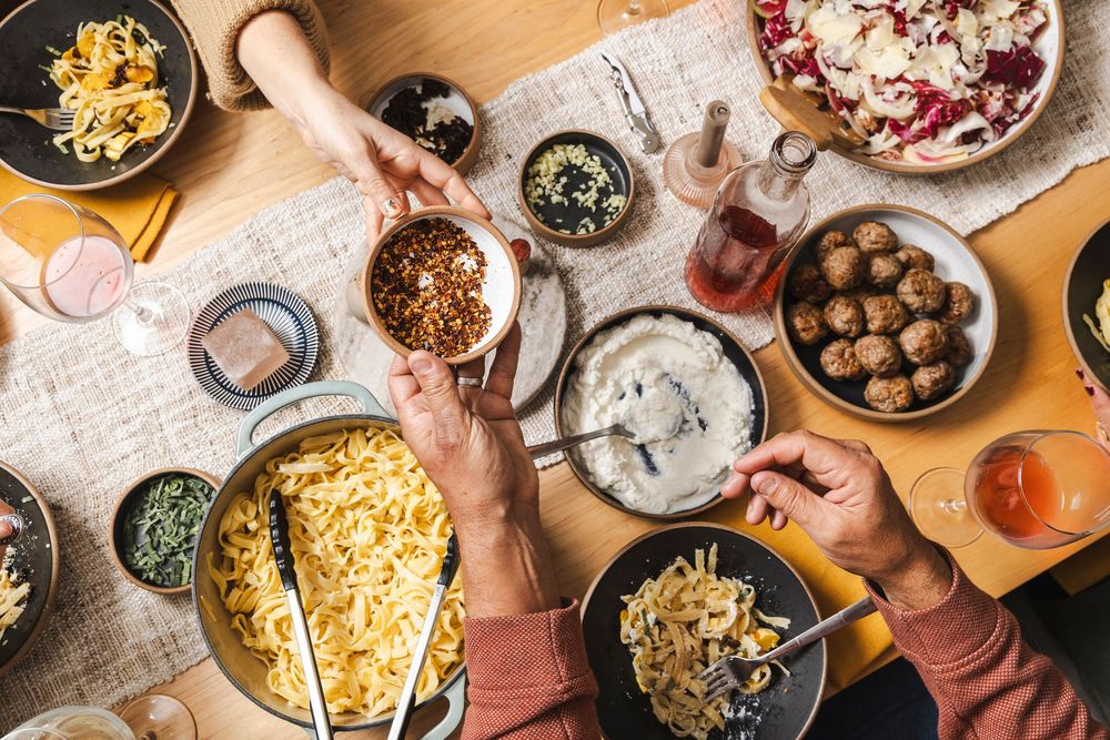 Birds-eye view of a communal dining table with hands reaching for shared plates and bowls of food.