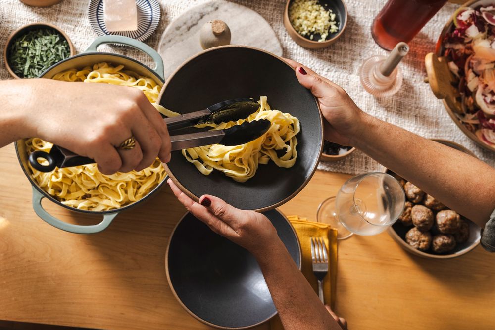 Overhead view of multiple hands sharing plates of food across a wooden table during dinner service.