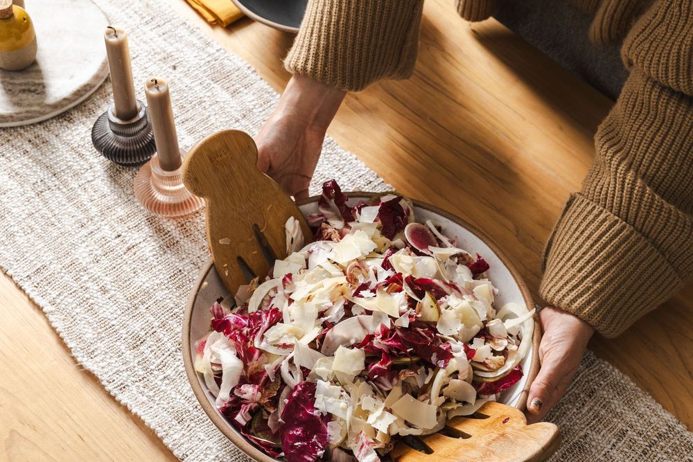 Hands serving a variety of dishes including pasta, salad, and appetizers on a rustic wooden dining table.