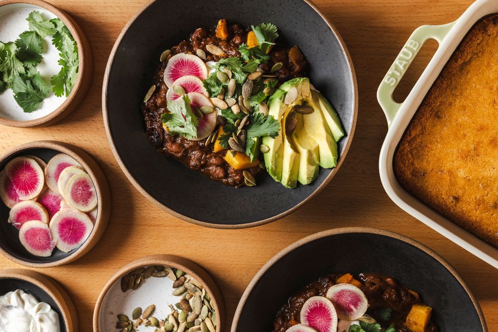 Overhead view of multiple restaurant dishes with vibrant garnishes and colorful plates on a wooden table surface.
