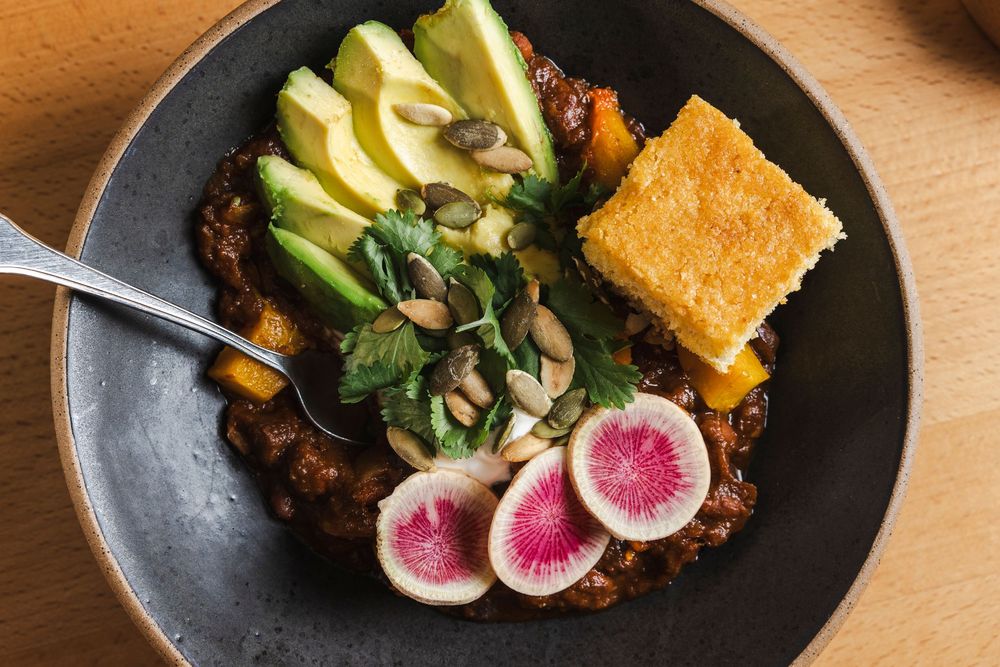 Black plate with colorful dish featuring watermelon radish, avocado, cornbread and mixed greens.
