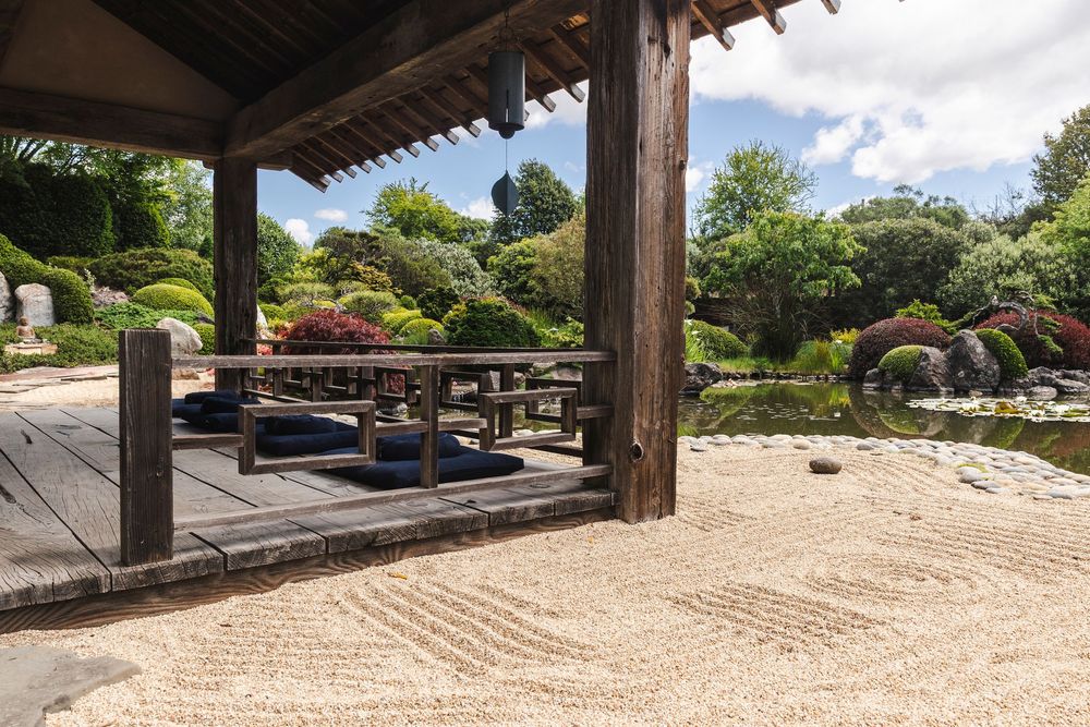 Peaceful stone garden with meticulously raked sand patterns and wooden pavilion in Japanese style architecture.
