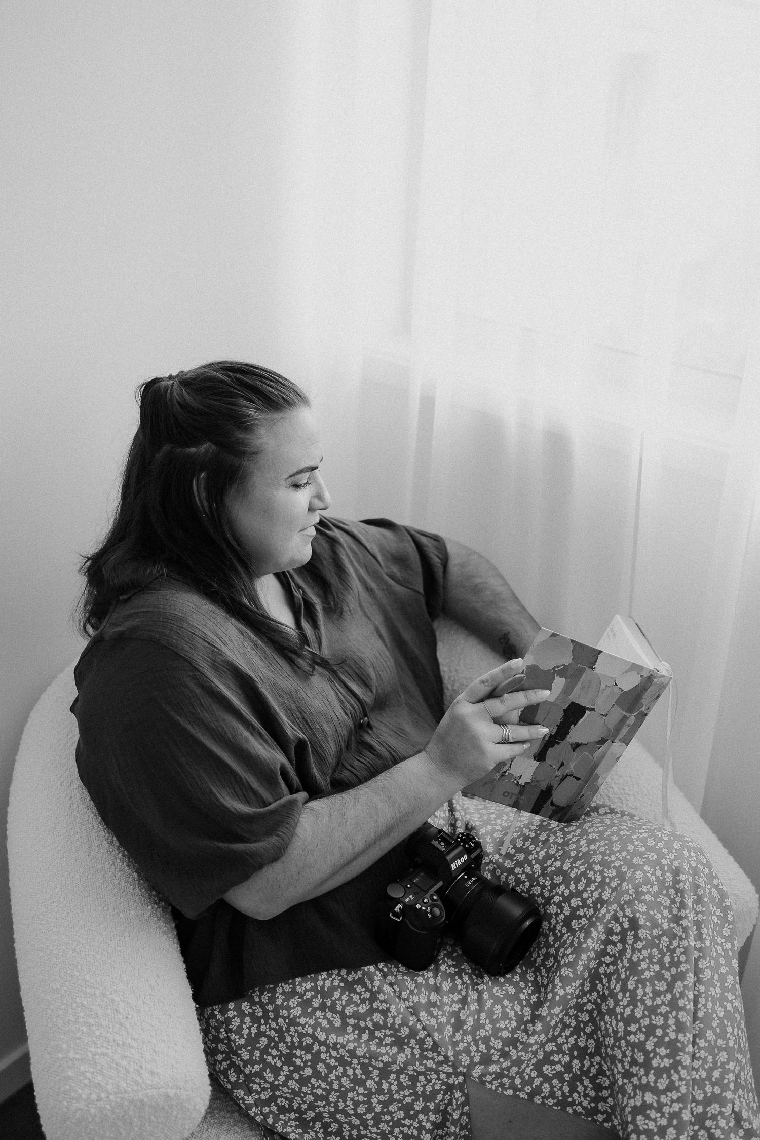 A person lies on a floral patterned couch reading a book in black and white photography.