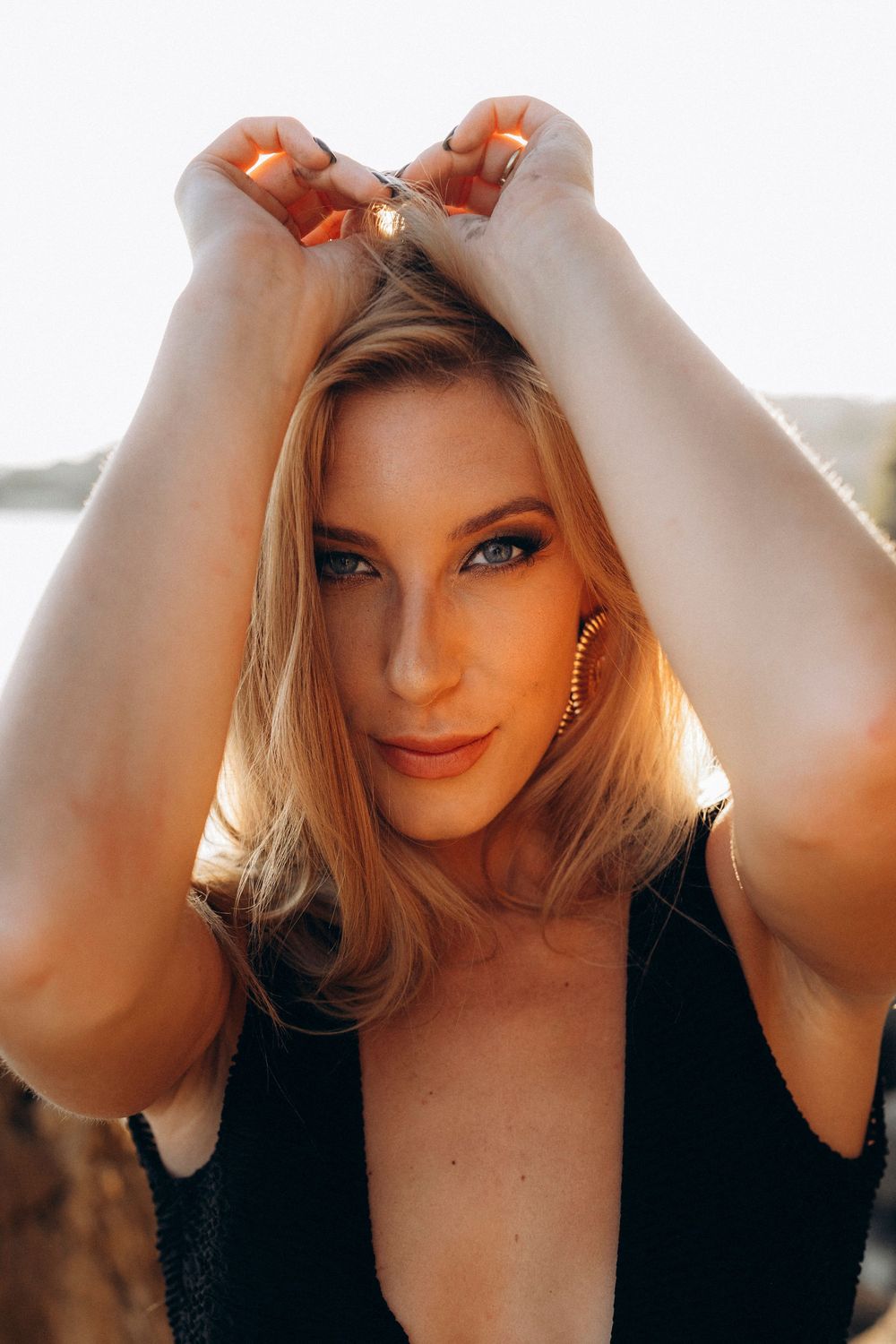 Portrait photo with warm golden sunlight showing blonde hair and dramatic eye makeup in a black top.