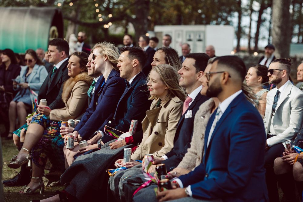 Wedding guests seated in rows smile and laugh during an outdoor ceremony.