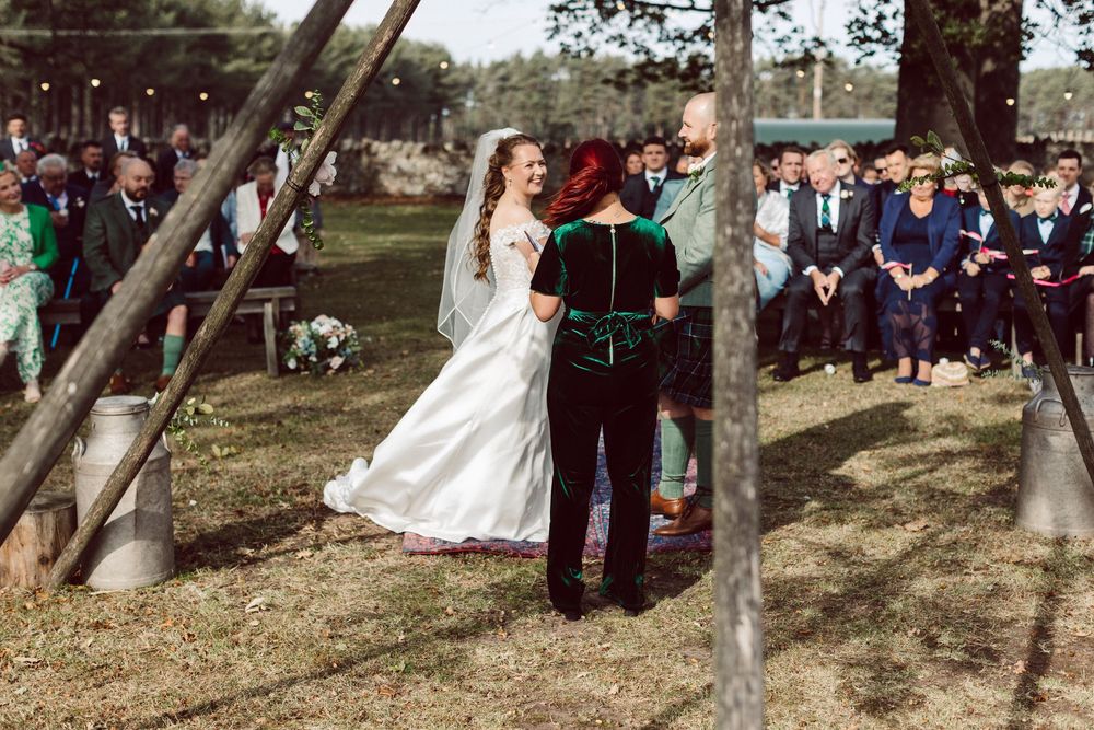 Wedding party gathers under shady trees for outdoor ceremony photos on a sunny afternoon.