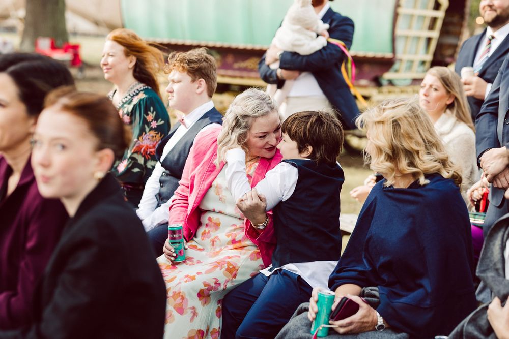 Wedding guests seated in rows smile and laugh during an outdoor ceremony.