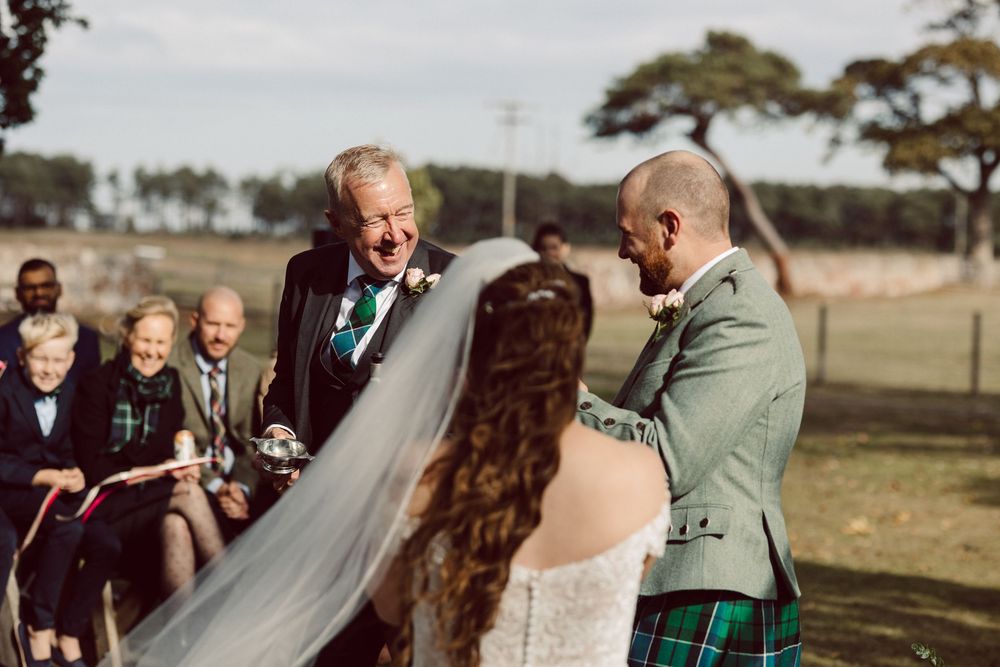 A joyful outdoor wedding ceremony with guests gathered in a field on a sunny day.