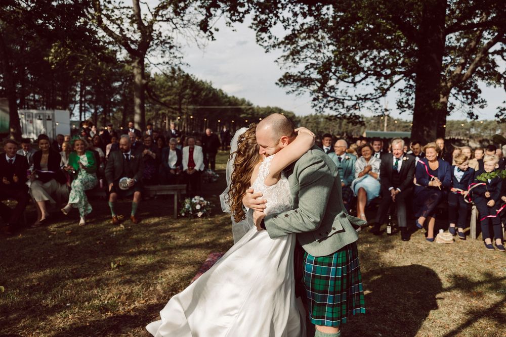 A couple shares their first dance surrounded by guests at an outdoor wedding reception.