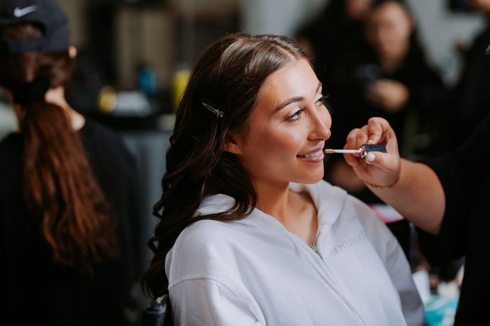Makeup artist applies cosmetics to a model wearing a white shirt in a professional setting.