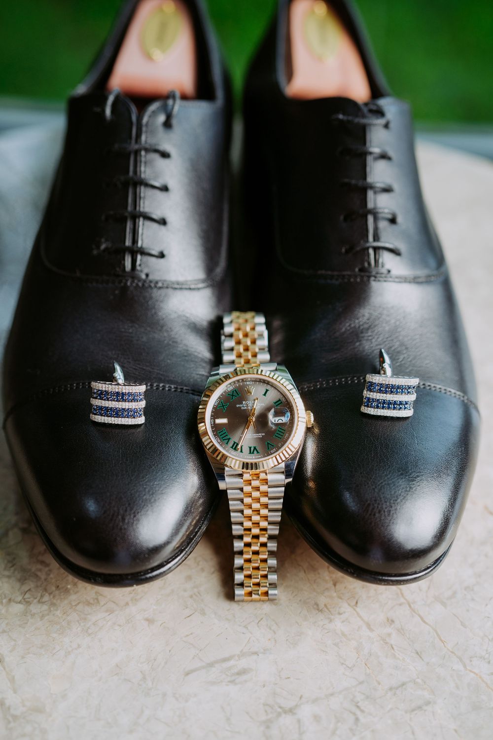 Elegant black leather dress shoes paired with a gold and silver luxury watch on white carpet.