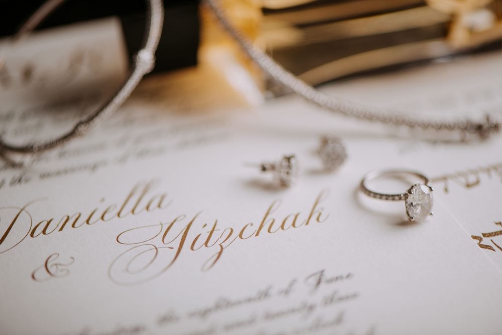 Elegant wedding invitation with calligraphy names and diamond engagement ring on white paper.