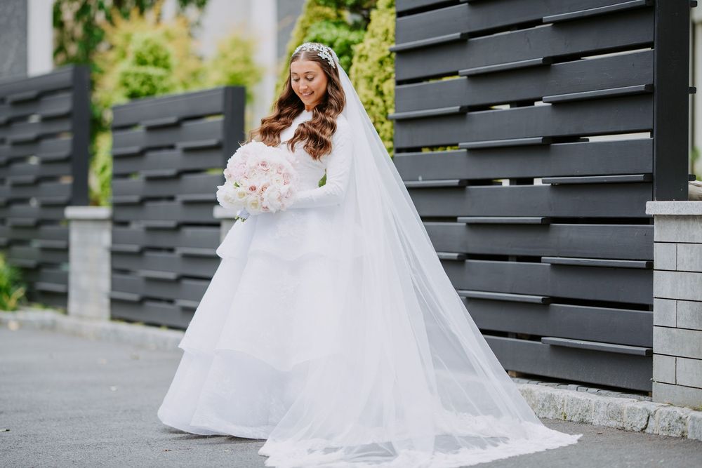 A bride in a flowing white wedding gown sits gracefully on outdoor stone steps surrounded by greenery.