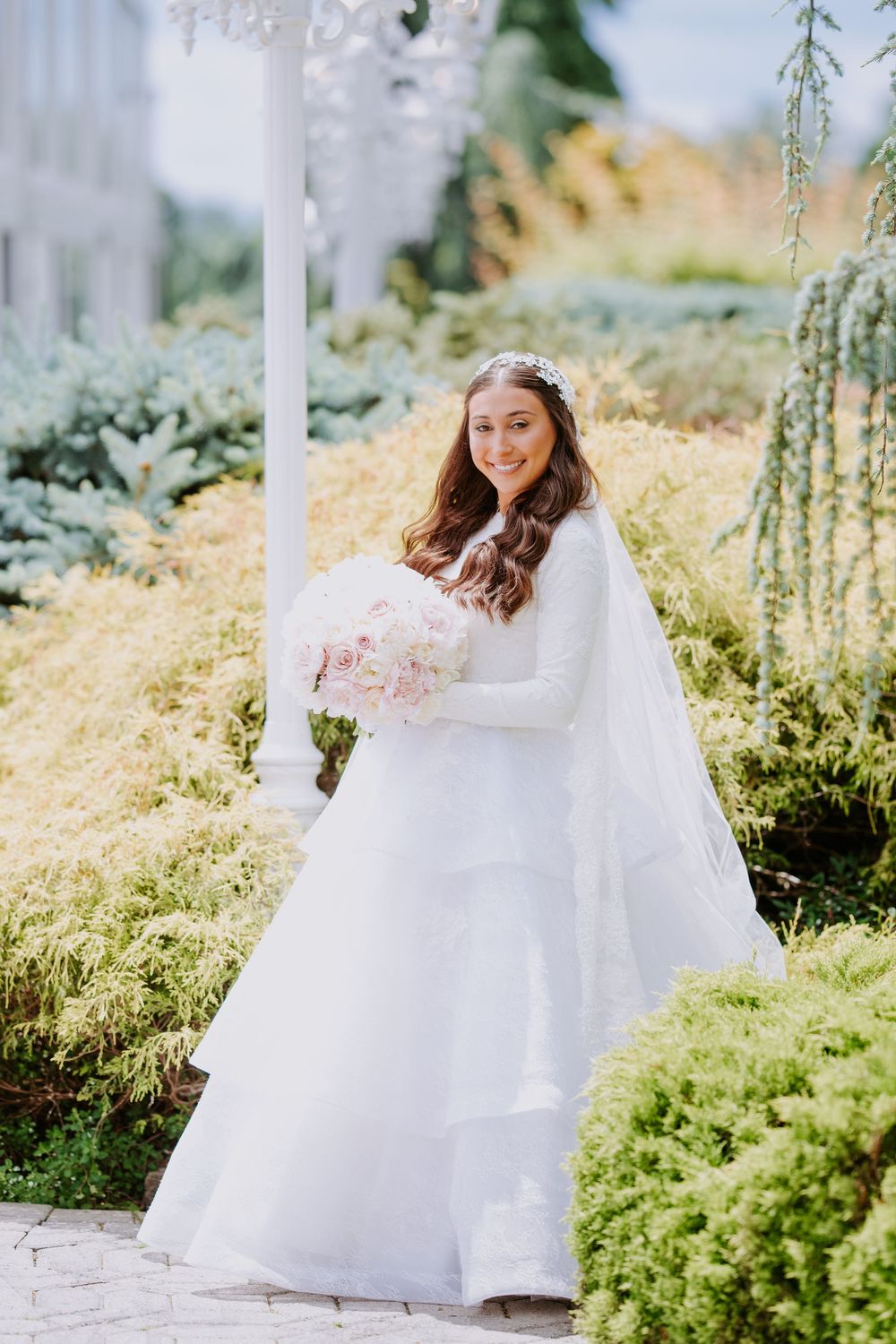 A young person in a flowing white dress twirls joyfully in a sunlit garden setting.