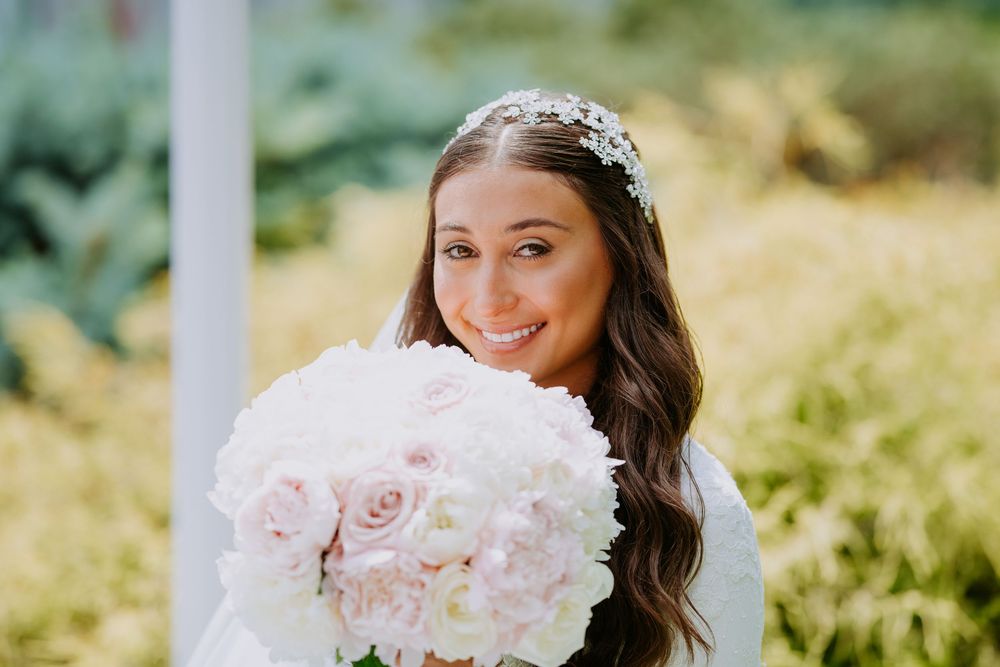 Bride holding a lush pink and white rose bouquet in an outdoor garden setting with natural sunlight.