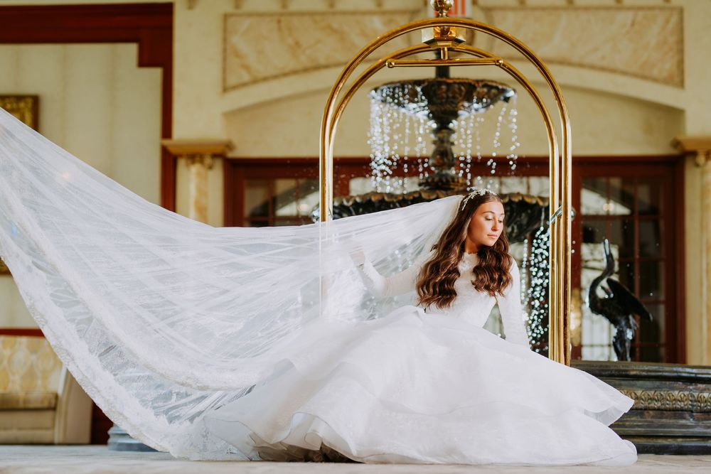 A flowing white wedding veil billows gracefully in the wind against an ornate architectural backdrop.
