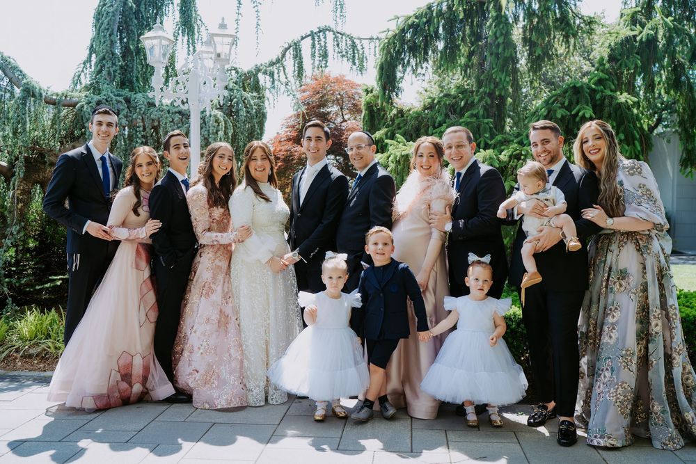 Wedding party poses together outdoors with weeping willow trees and church spires in the background.