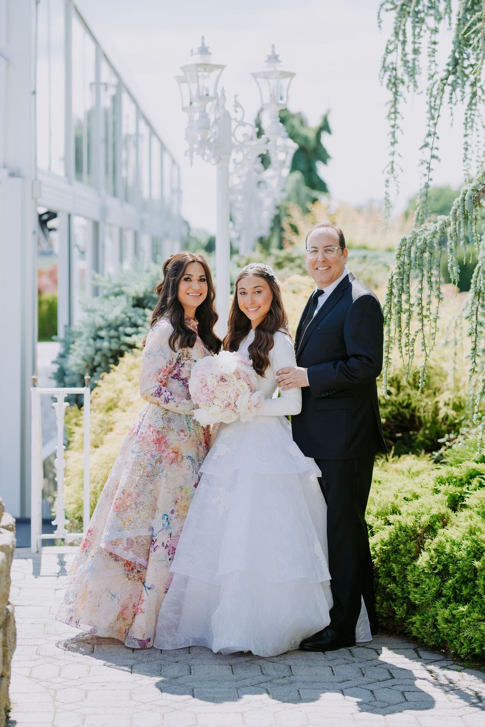 Wedding party poses together in a garden setting with white dresses and formal attire.