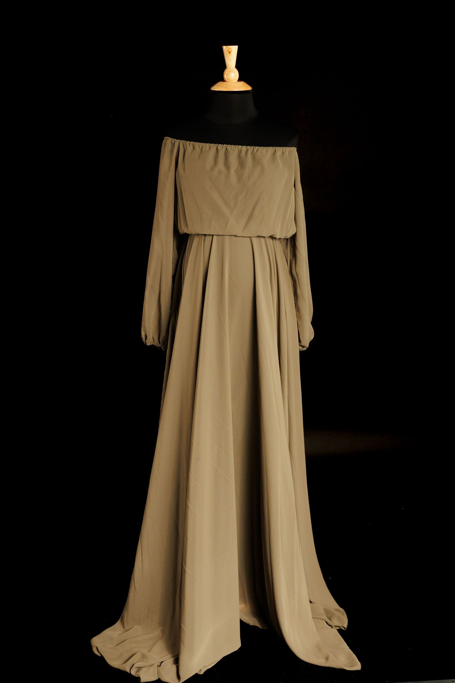 Elegant off-shoulder beige maxi dress with long sleeves and flowing skirt displayed on a black mannequin stand.