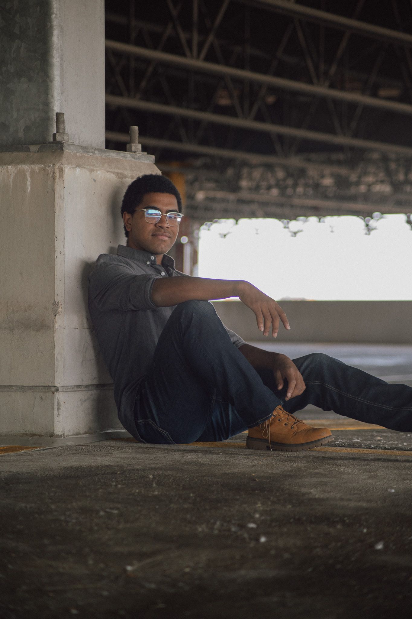 Person wearing sunglasses relaxing on the ground in an urban parking structure.