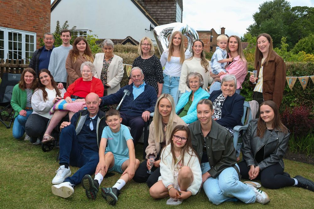 Large multigenerational family group posing together outdoors in a garden during a sunny celebration gathering.