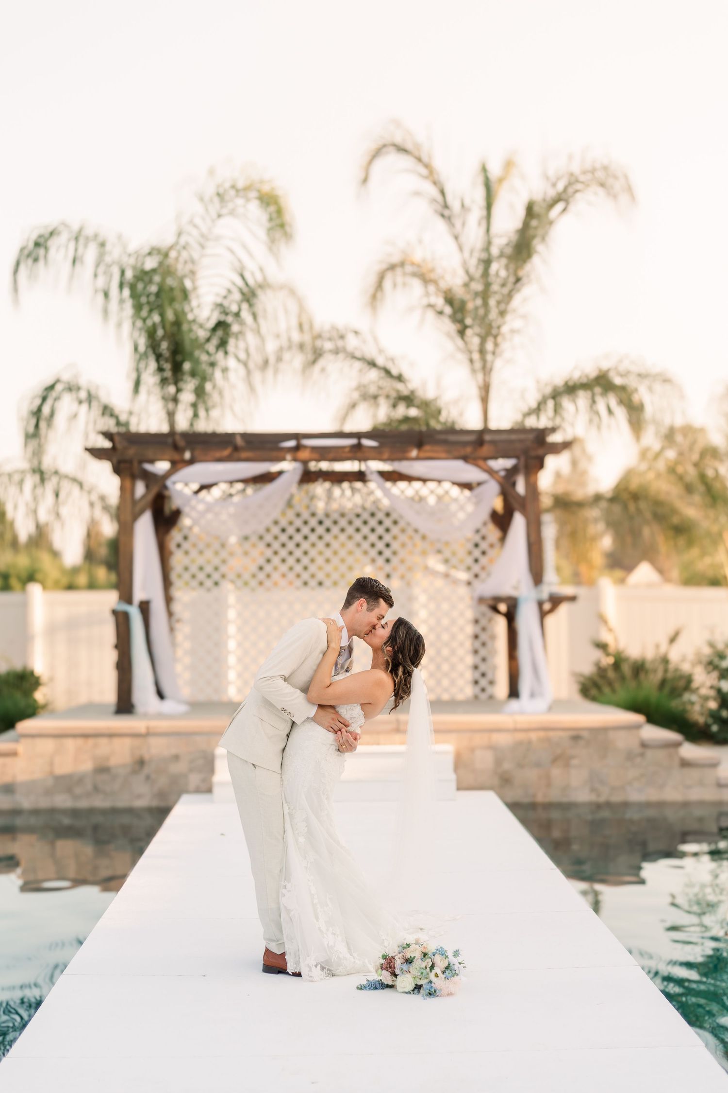 Elegant wedding photos taken beside a pool with white lattice backdrop and palm trees.