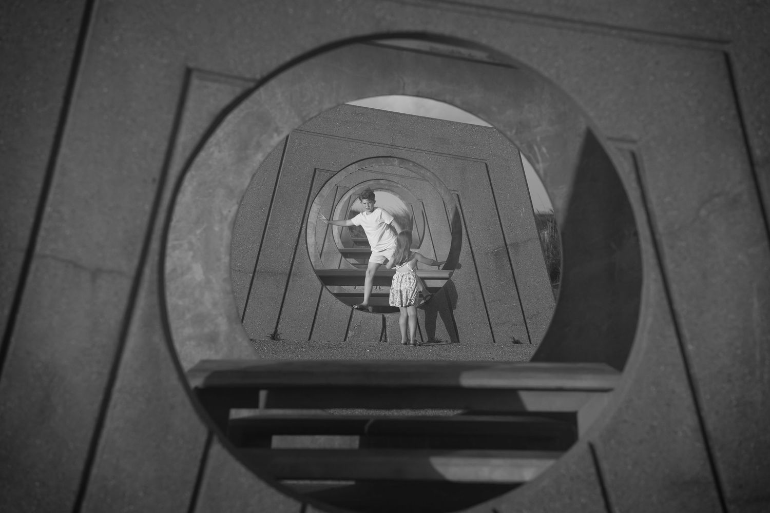 Black and white photo of children standing inside a geometric tunnel structure at Matagorda Beach, Texas
