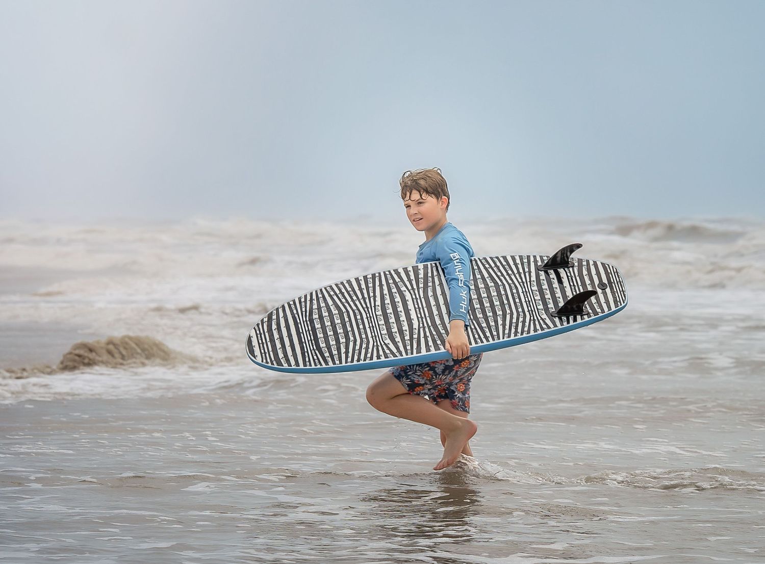 Child walking through the surf with a surf board in Matagorda, TX at Matagorda Beach.