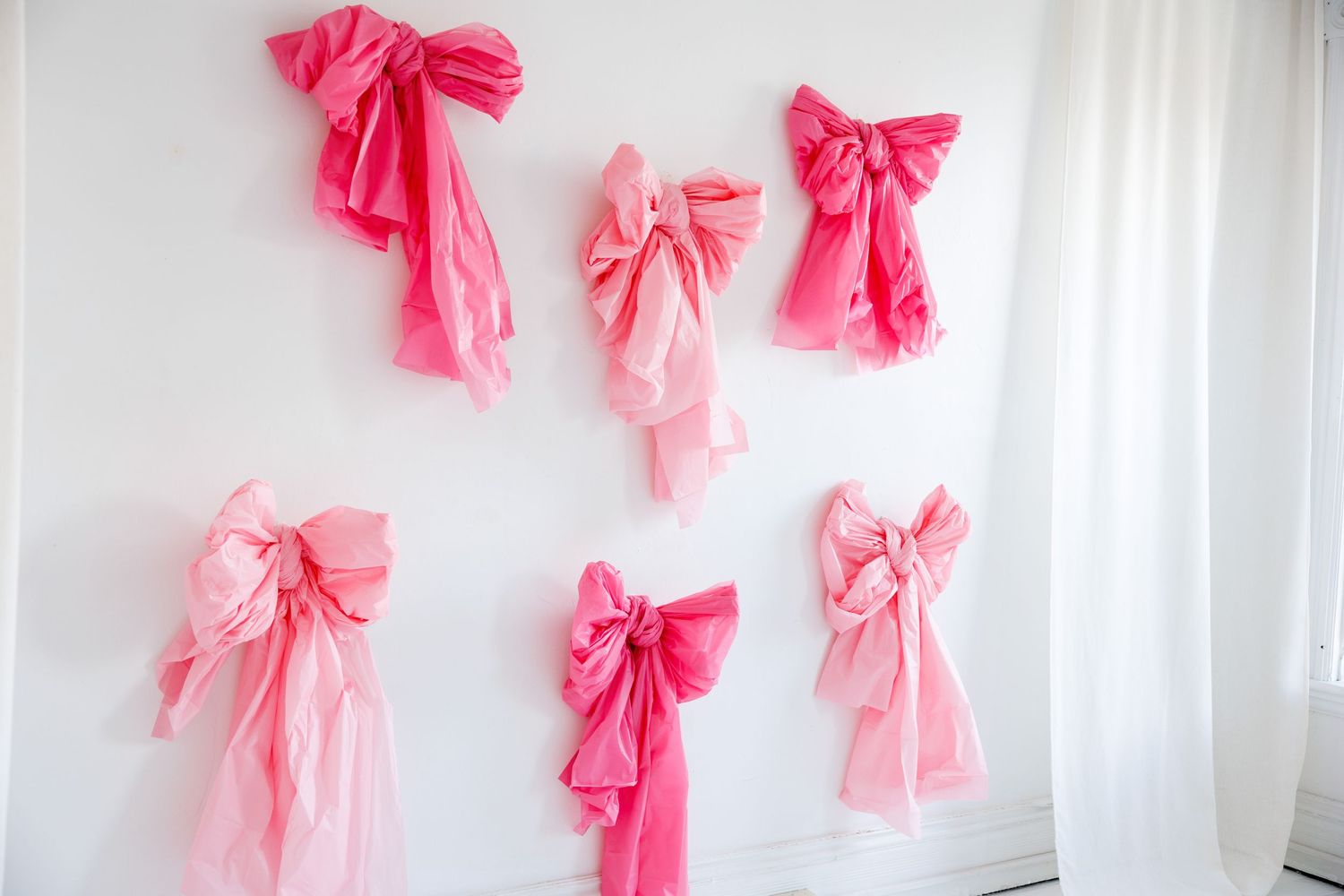 A photographer holding a camera against a white wall decorated with pink paper bows.