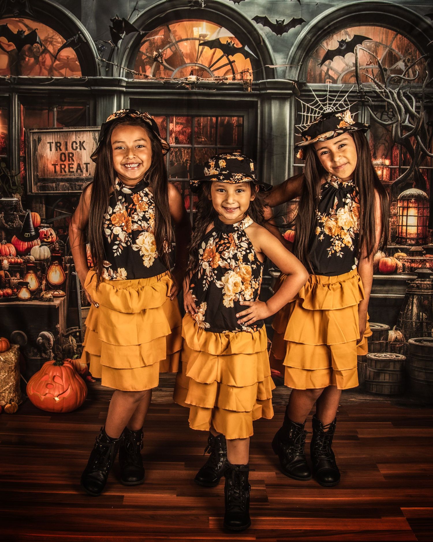Three children in matching yellow ruffled outfits pose in spooky Halloween setting.