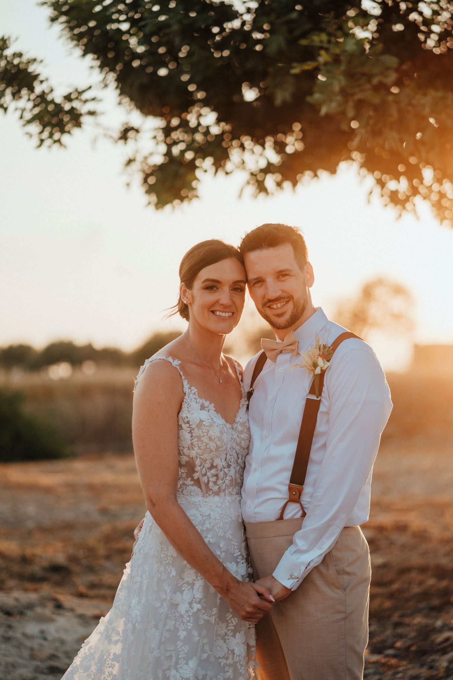 A romantic wedding moment captured among lush greenery with two people embracing in formal attire.