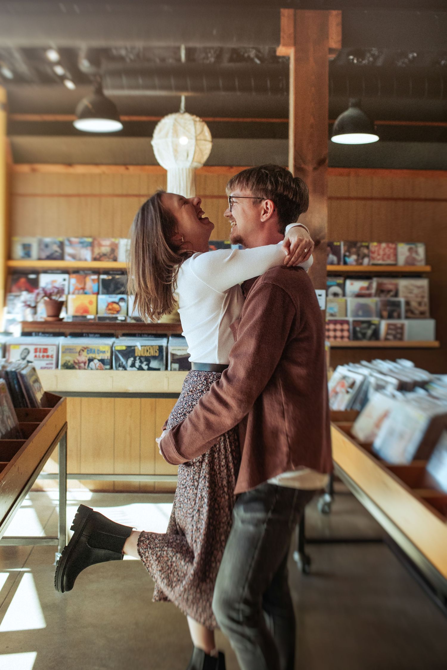 A couple in brown clothing share an intimate dance moment in a vinyl record store with wooden walls and vintage decor. Indianapolis, Indiana