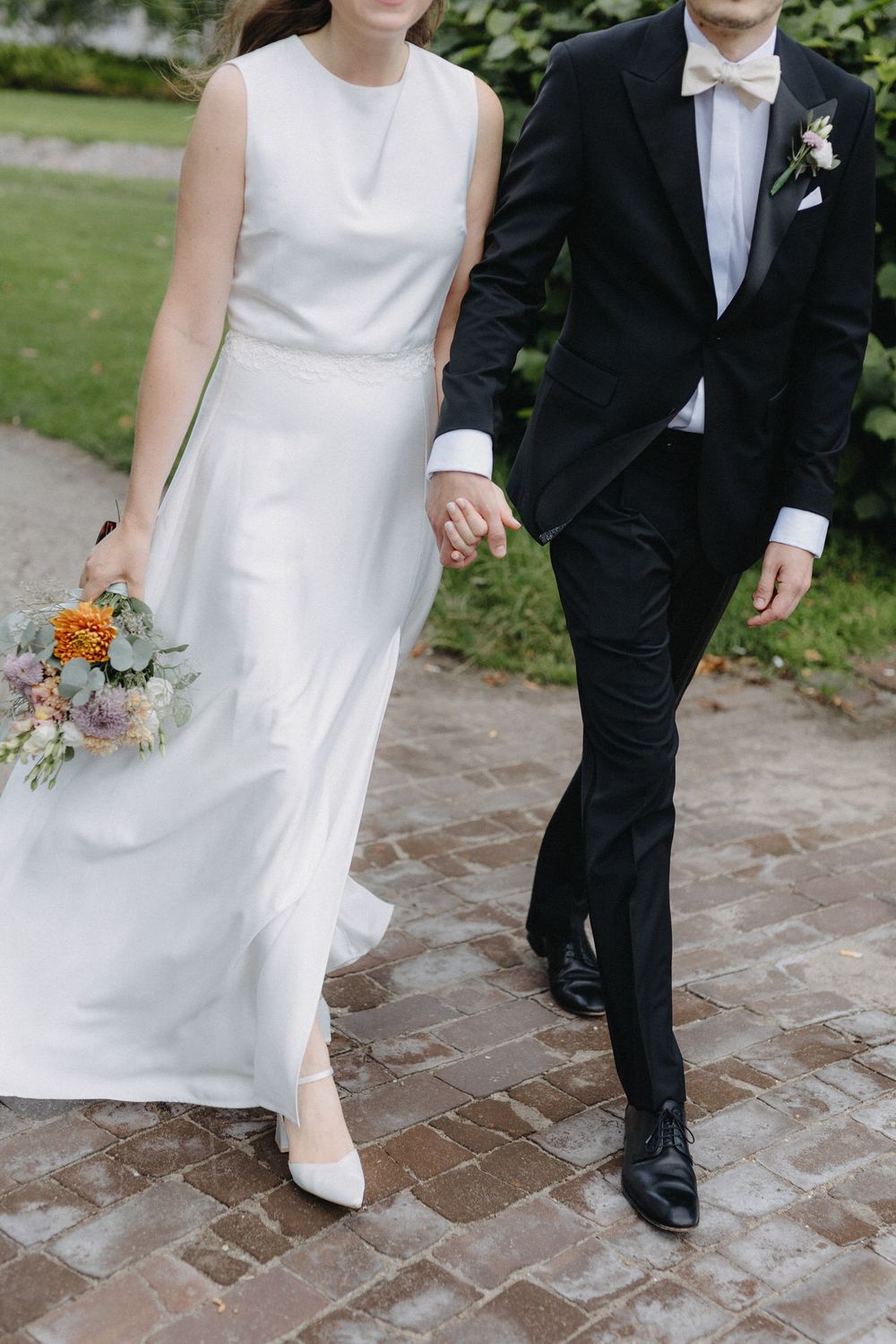 Close-up shots of bride and groom walking together on brick path showing white wedding dress and black tuxedo details.
