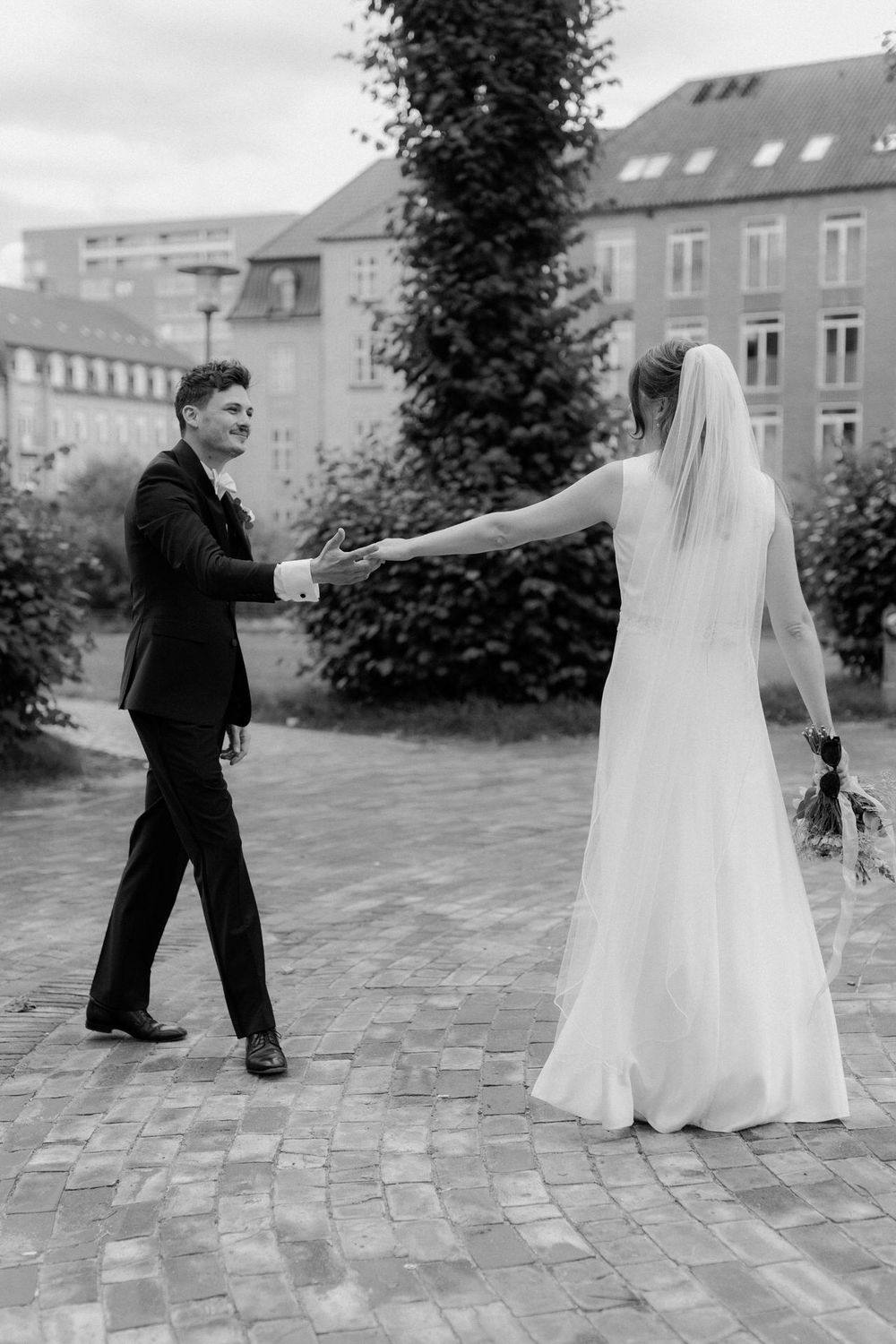 A bride and groom share their first dance outdoors on a brick patio with buildings in the background.