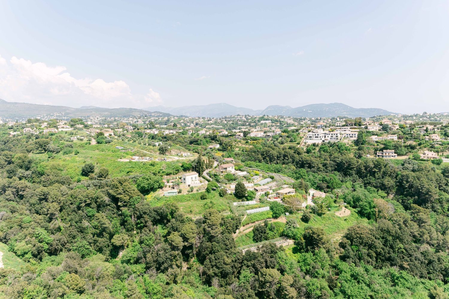 Panoramic aerial view of a green hillside town with scattered buildings and lush vegetation in a mountainous region.