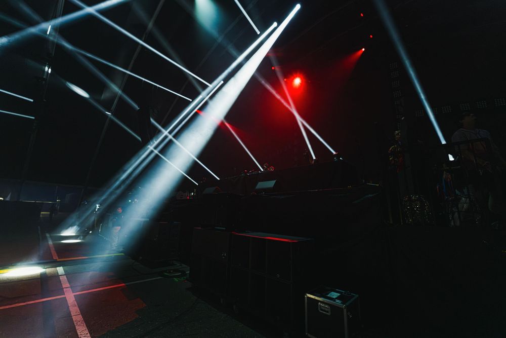 Dramatic light beams in red and white pierce through a dark space creating an atmospheric nightclub scene.