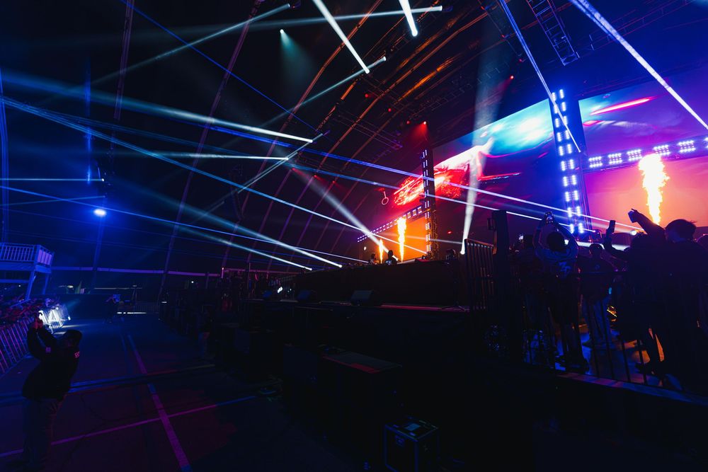Colorful laser beams illuminate a dark concert venue with blue and purple lights creating a dynamic atmosphere.