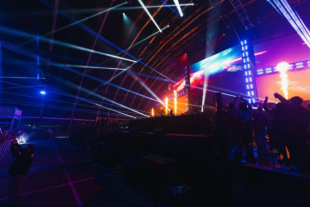 Vibrant blue and pink laser beams illuminate a dark concert venue with dramatic lighting effects.