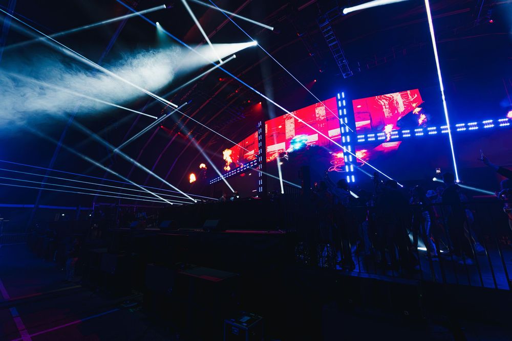 Concert stage lighting display with blue and red beams cutting through dark atmosphere during live performance.