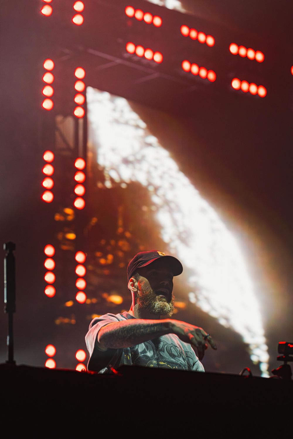 Concert performers on stage silhouetted against dramatic red lighting and bright white spotlights during a live show.